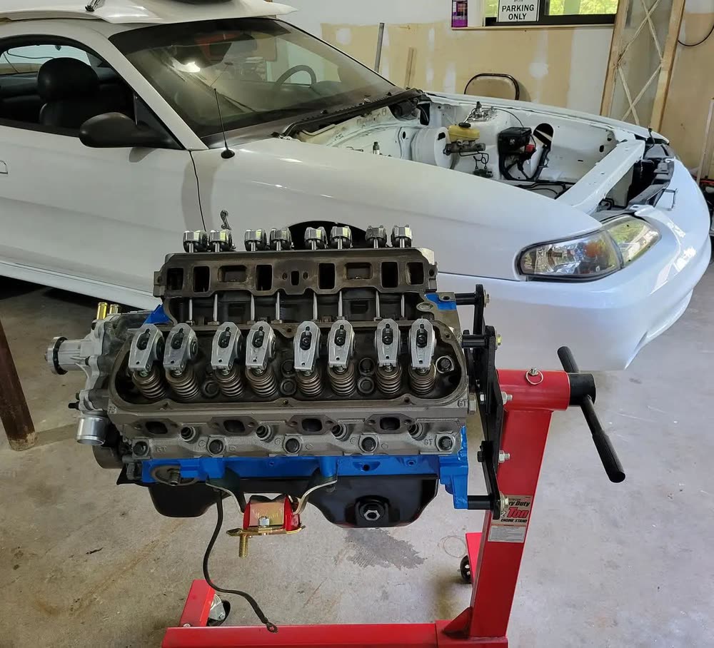 Replacement engine mounted on a stand in front of the vehicle it is going into