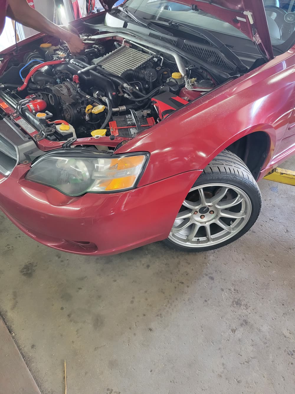 Red Subaru with its hood open for engine inspection in the shop